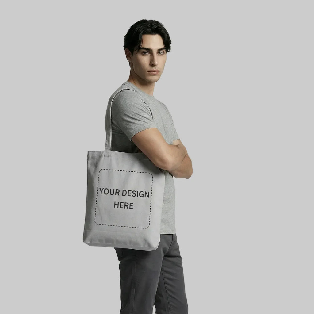 Man holding a gray tote bag with 'Your Design Here' text on a plain background